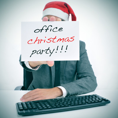 a man sitting in his desk with a santa hat holding a signboard with the text office christmas party written in it